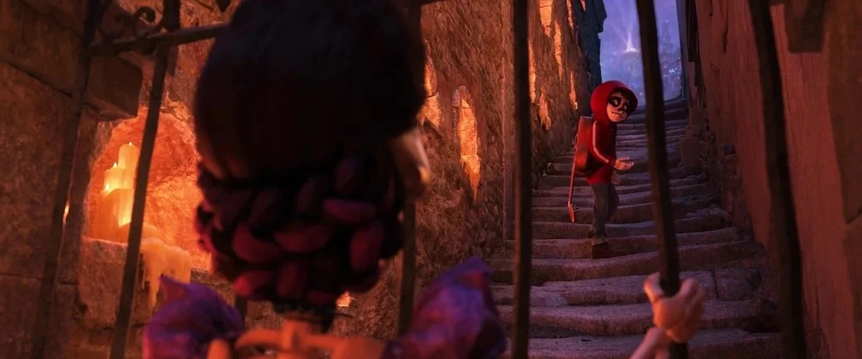 Coco (2017) movie still: medium — A dark stone staircase at night is flanked by alcoves containing burning white candles. A young boy in a red…