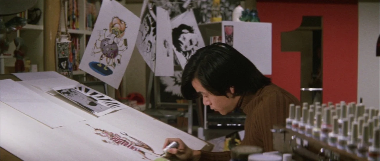Godzilla Vs Gigan (1972) movie still: medium — An artist works in a brightly lit studio filled with hanging character illustrations. The subject…