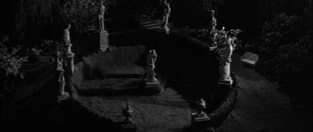 The Innocents (1961) movie still: establishing — A circular garden at night features stone statues atop pedestals encircling a central clearing. A…