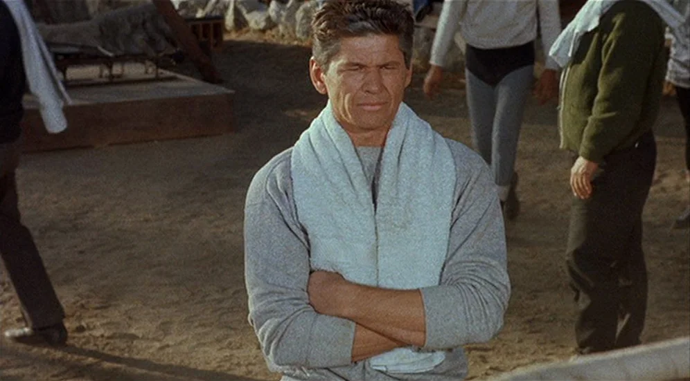 Kid Galahad (1962) movie still: medium — A dusty outdoor training yard features dirt ground and scattered equipment in the background. A middle-aged…