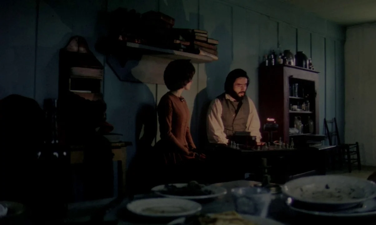 Kamouraska (1973) movie still: medium — A dark, wood-paneled room features period furniture and a set table in the foreground. A man and woman sit…