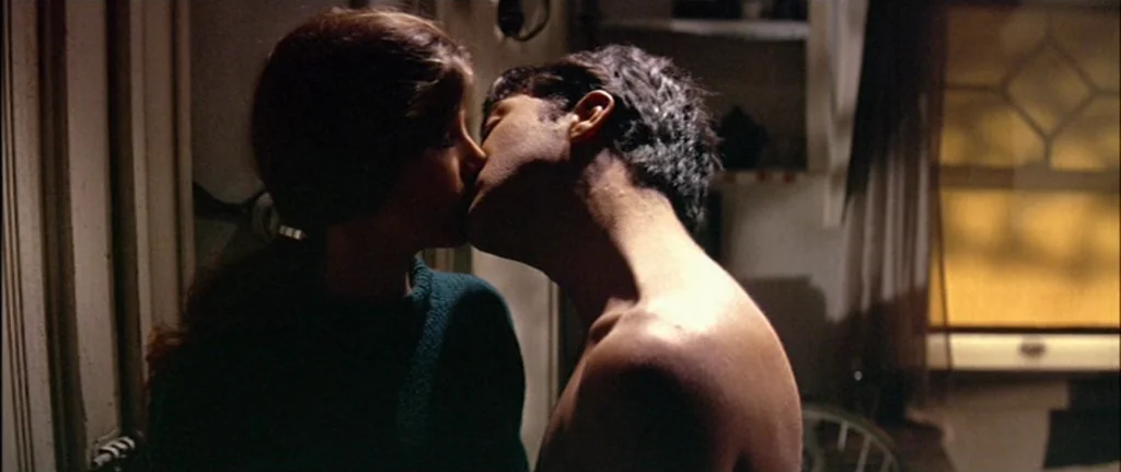 The Graduate (1967) movie still: medium — A dimly lit room features a window with a diamond-patterned grid in the background. A man and woman are…
