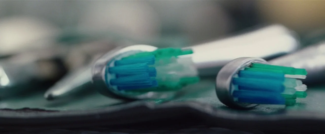 Hanna (2011) movie still: closeup — Two electric toothbrush heads with blue and green bristles lie on a textured mat. They are positioned in the…