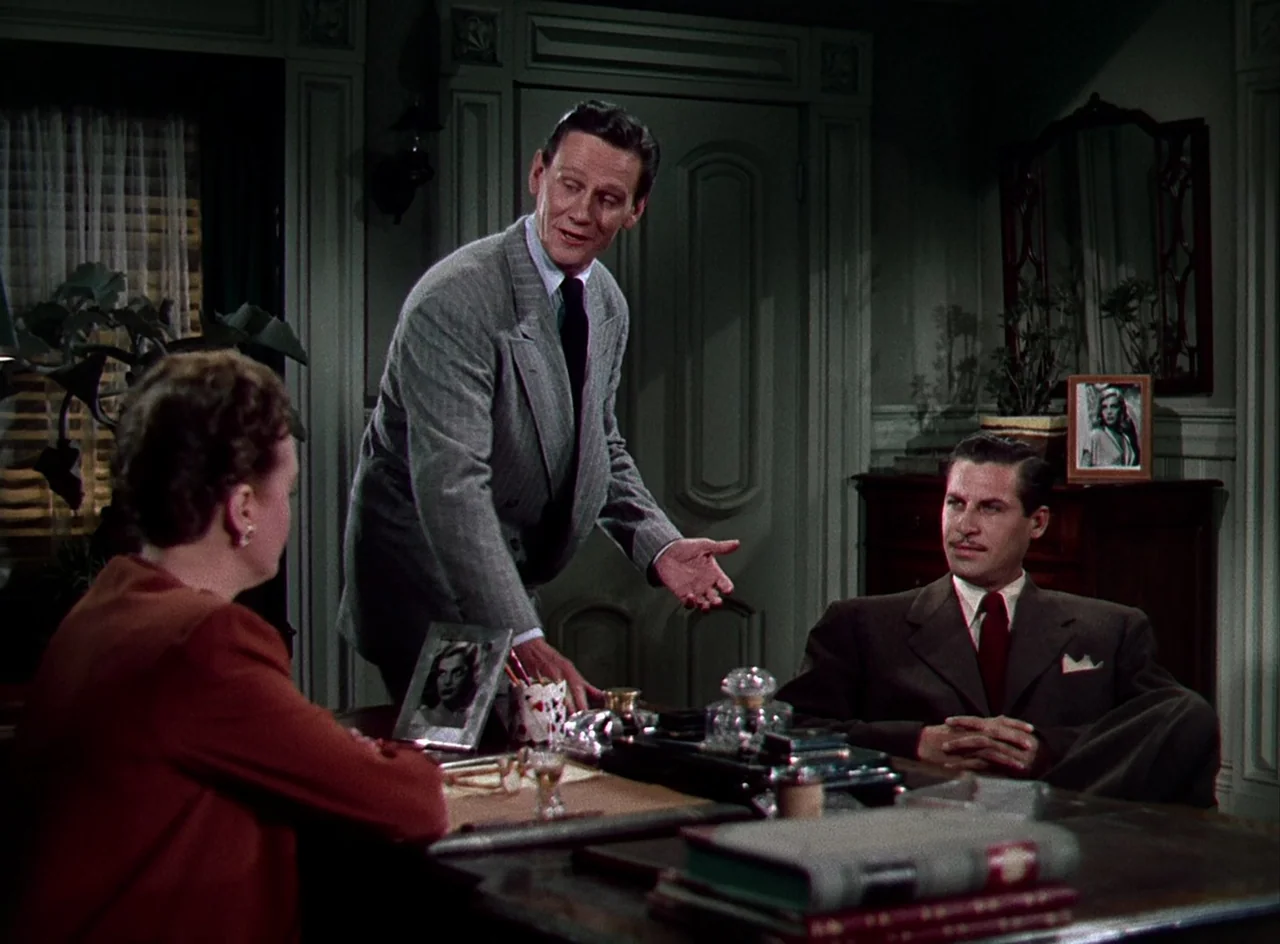 Desert Fury (1947) movie still: medium — A traditional wood-paneled room contains a desk with various personal items and photographs. Three…