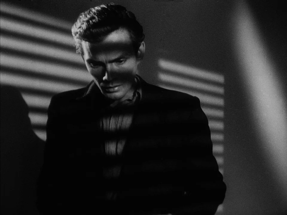 It Rains On Our Love (1946) movie still: medium — A man stands in a dimly lit space with high-contrast shadows on his face. He is illuminated by…