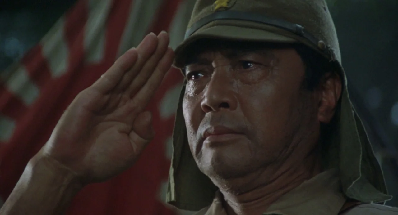 Godzilla vs. King Ghidorah (1991) movie still: closeup — An outdoor battlefield setting features a red and white flag partially obscured behind him.…