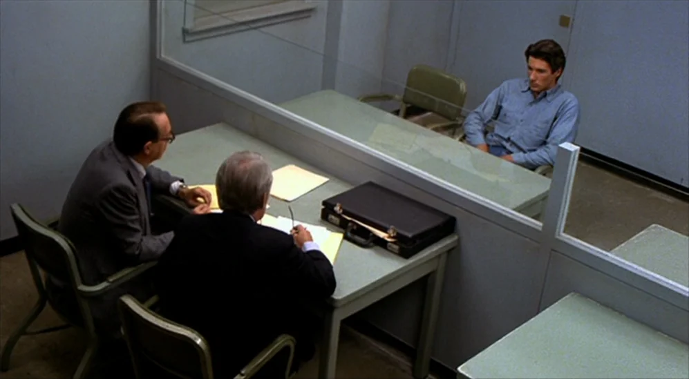 American Gigolo (1980) movie still: wide — A stark, institutional visitation room featuring a transparent glass divider separating two distinct…