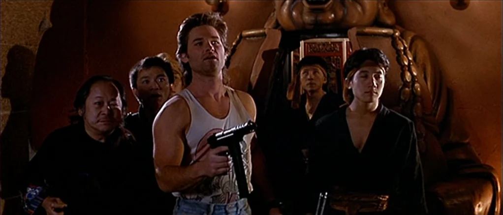 Big Trouble in Little China (1986) movie still: medium — The group stands in a dimly lit, brown-toned interior featuring a large carved statue. A…