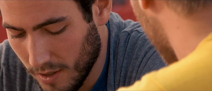 This Movie Is Broken (2010) movie still: closeup — Two men face each other inside a room with soft ambient light. The man on the left listens with…