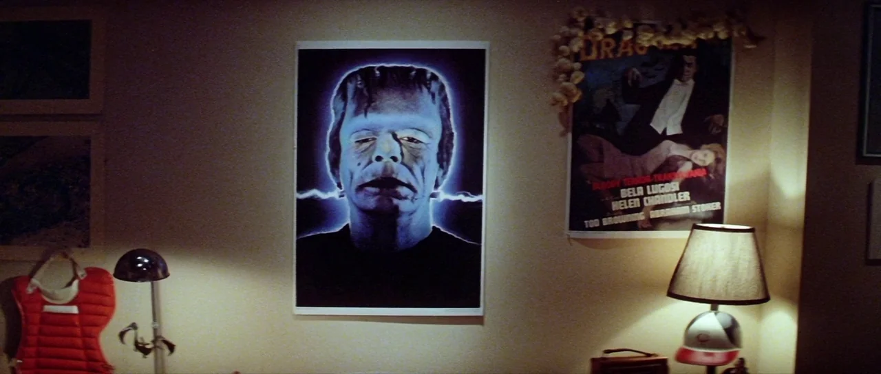 The Funhouse (1981) movie still: establishing — A residential bedroom wall features a large Frankenstein movie poster and a smaller Dracula poster.…