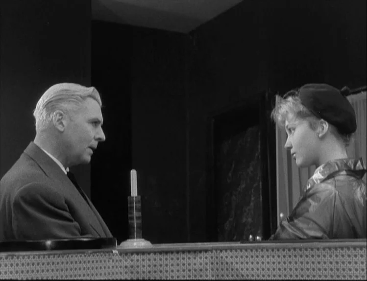 Bob le Flambeur (1956) movie still: medium — A dark diner booth interior with a patterned table edge in the foreground. An older man in a suit faces…