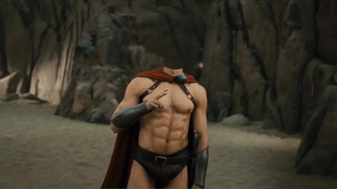 Meet the Spartans (2008) movie still: medium — A muscular man stands in front of a jagged stone cliffside. He wears a red cape and leather armor…
