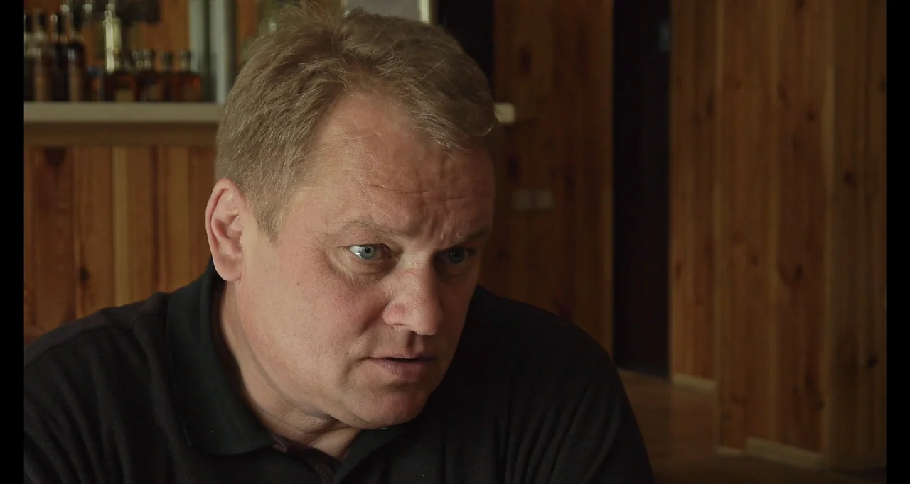 Chernobyl's Café (2016) movie still: medium — A room with wooden paneled walls provides a neutral indoor setting. A middle-aged man stands and looks…
