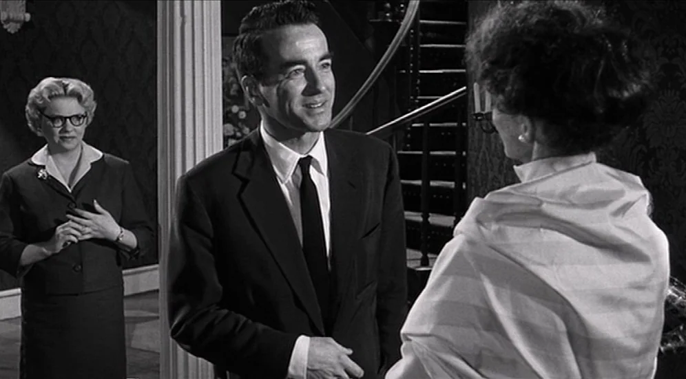 Suddenly, Last Summer (1959) movie still: medium — A grand residential foyer features dark patterned wallpaper and an ornate wooden staircase. A man…