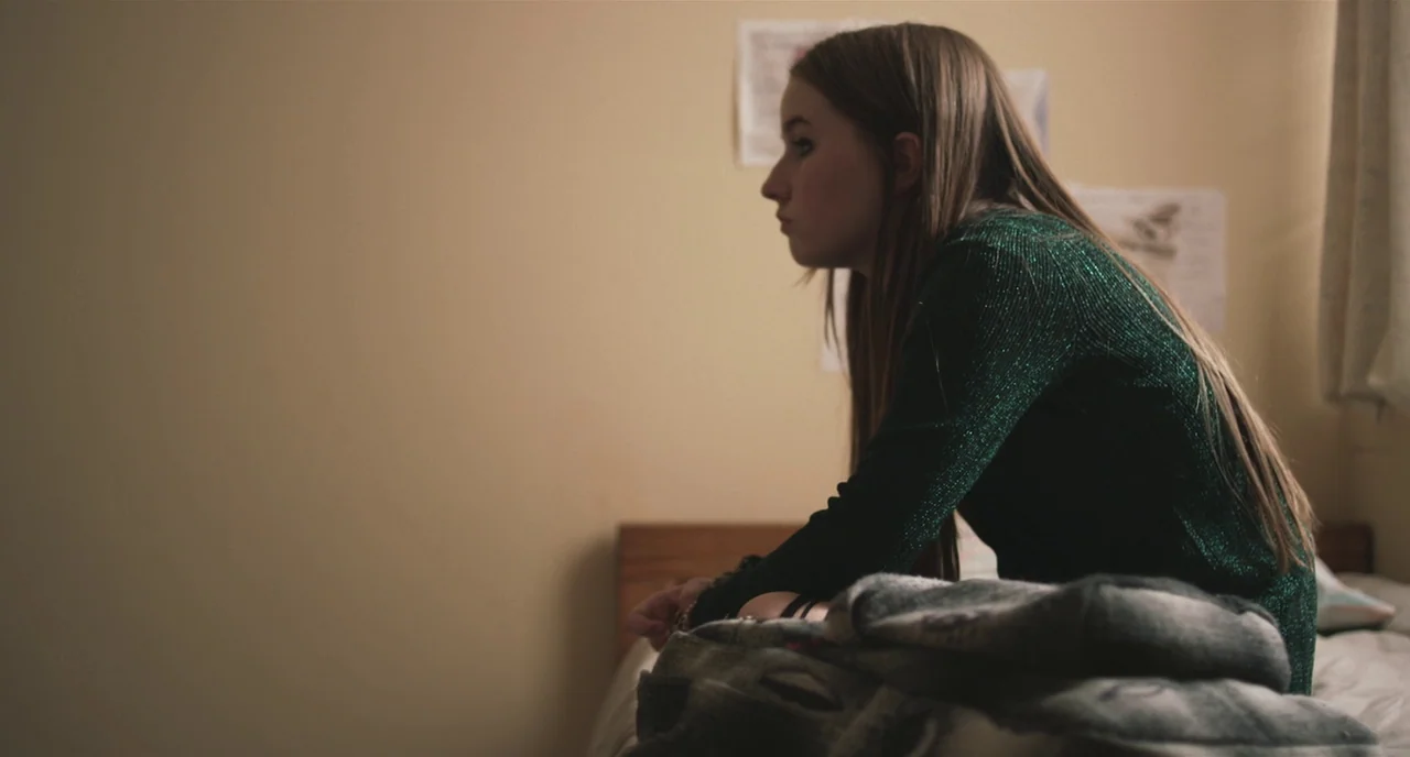 Short Term 12 (2013) movie still: medium — A plain bedroom features beige walls adorned with small paper notices or posters. A young woman in a…