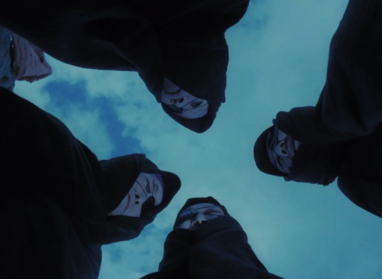 Pastoral To Die In The Country (1974) movie still: medium — Four individuals wearing black hoods and painted faces stand in a circle. They look down…