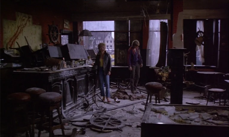 Spetters (1980) movie still: wide — A destroyed bar interior features scattered debris, overturned stools, and a detached wooden helm. Two…
