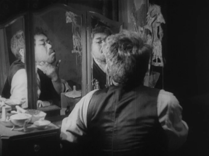 Drunken Angel (1948) movie still: medium — A man sits before a vintage tri-fold mirror on a wooden furniture piece. He looks at his reflection while…