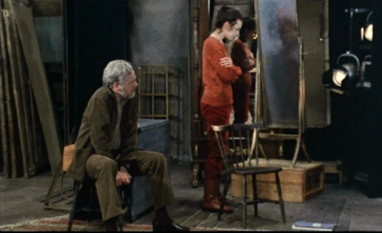 After The Rehearsal (1984) movie still: medium — A cluttered room containing stacked boards, a wooden chair, and a standing mirror. An older man…
