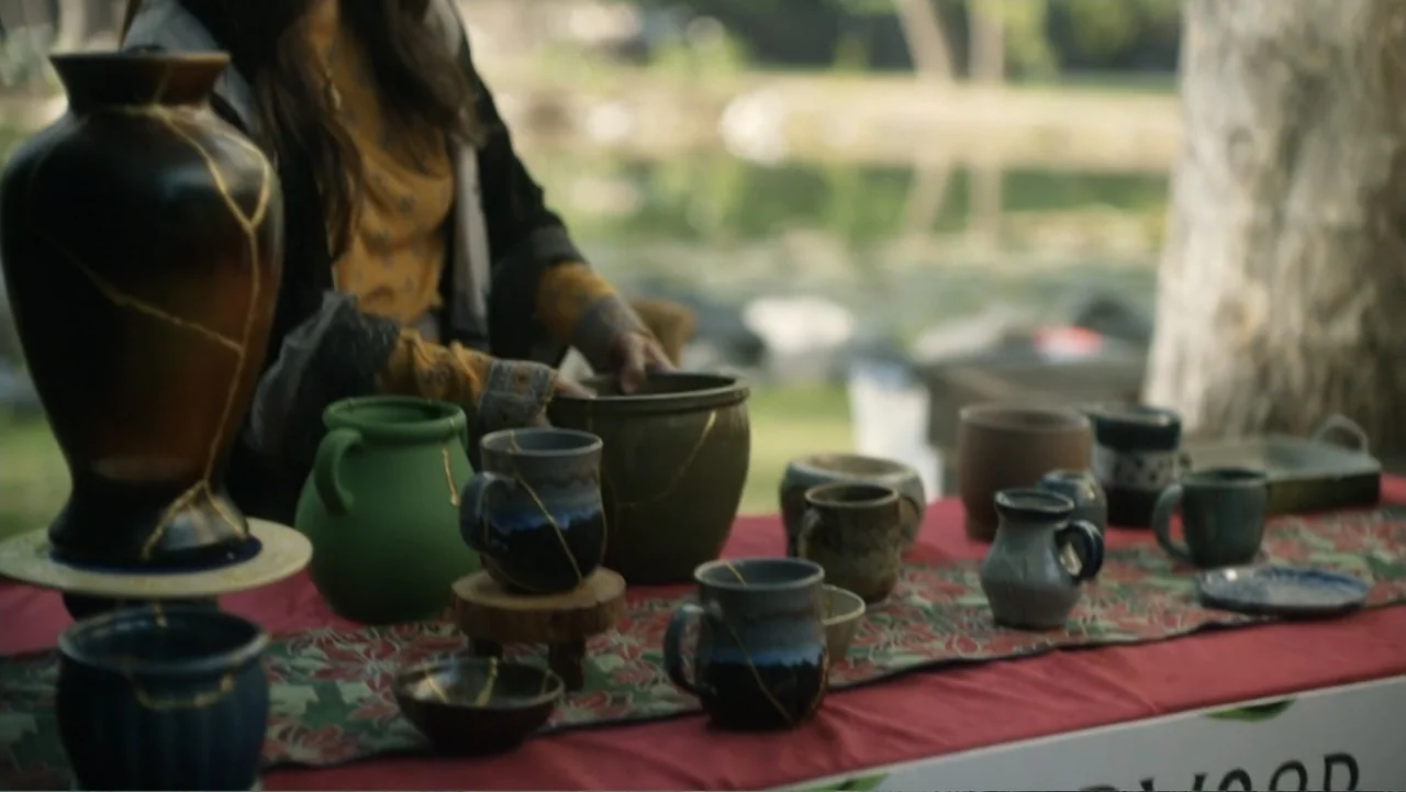 A Carpenter Christmas Romance (2024) movie still: medium — A wooden table set up outdoors displays numerous hand-crafted ceramic mugs and vases. A…