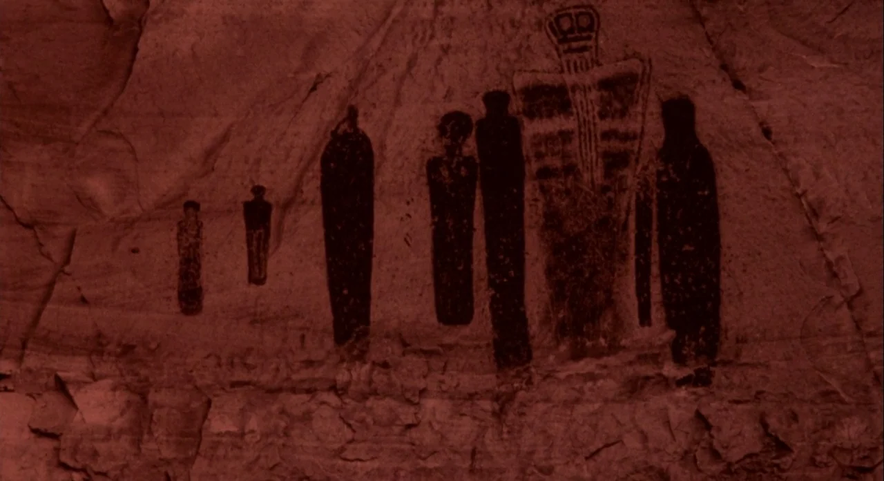 Koyaanasquatsi (1982) movie still: medium — Ancient petroglyphs of stylized human figures are painted on a textured canyon rock wall. A large…