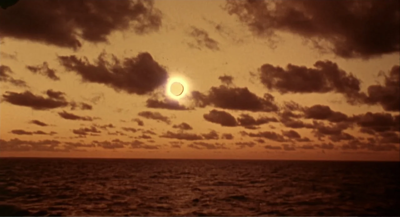 Hercules (1983) movie still: establishing — A vast expanse of ocean meets the horizon under a heavily clouded sunset sky. The sun is visible as a…