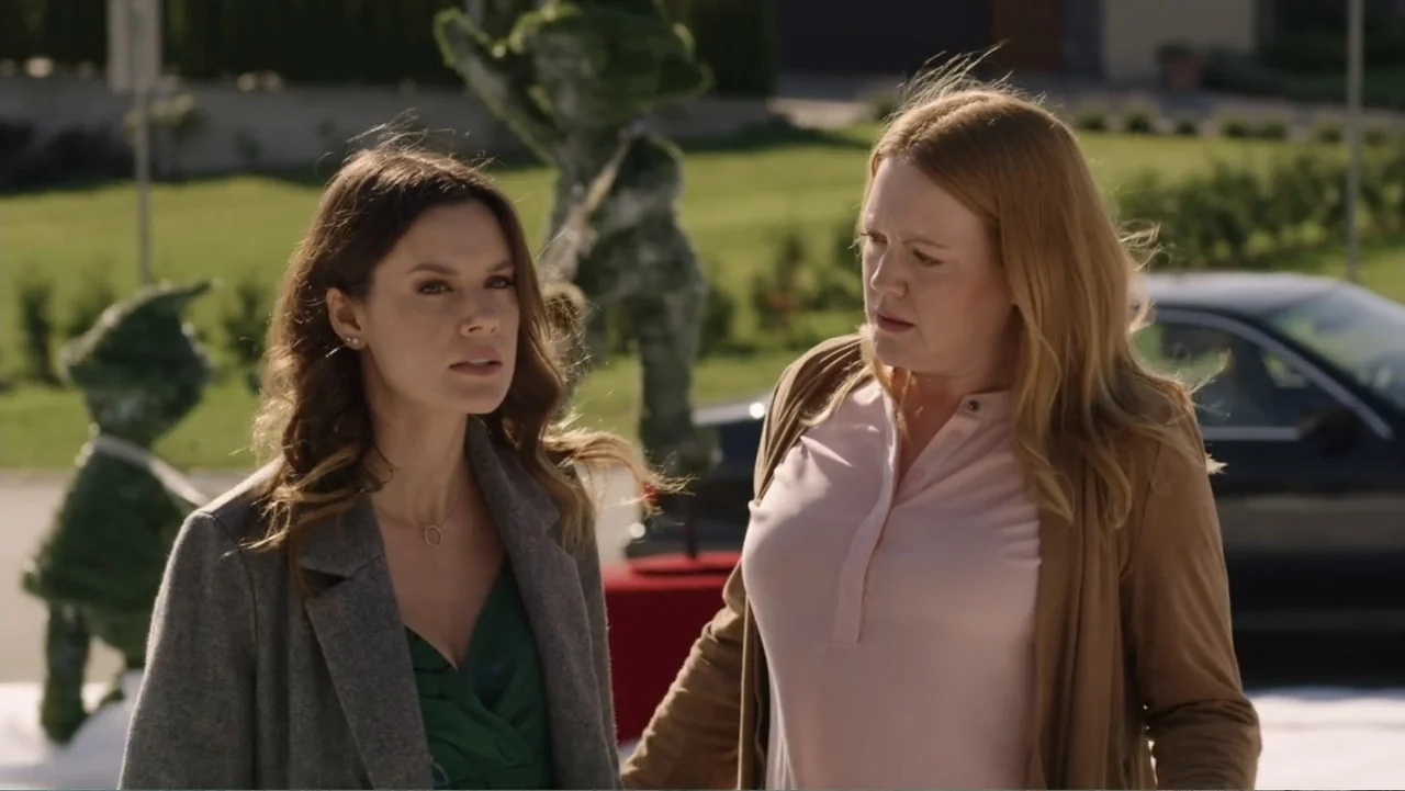 Always and Forever Christmas (2019) movie still: medium — Two women stand on a manicured green lawn in front of a house. One woman looks at her…