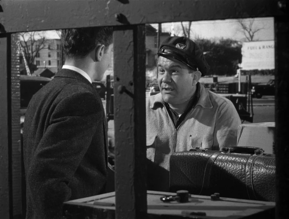 Strangers on a Train (1951) movie still: medium — A man in a work jacket speaks to a young man in a suit. They stand near a luggage trunk within an…