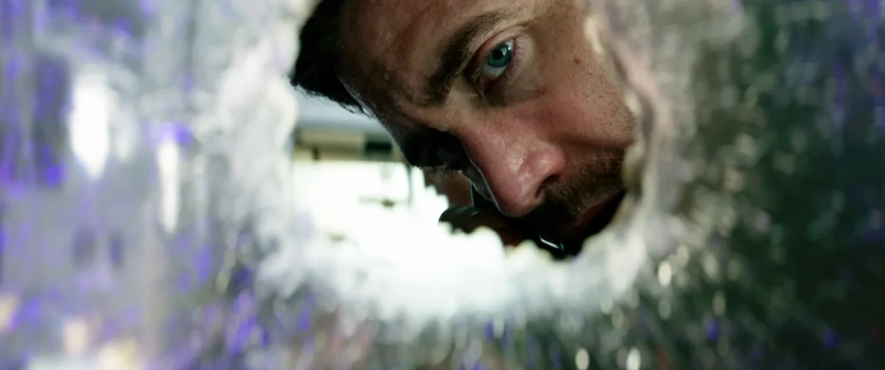 Ambulance (2022) movie still: closeup — A man's face appears through a circular fracture in a sheet of glass. He peers forward with his blue eyes…