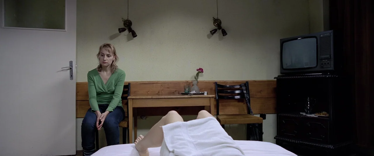 4 months, 3 Weeks and 2 Days (2007) movie still: medium — A spartan room features pale green walls, wooden furniture, and a television on a cabinet.…