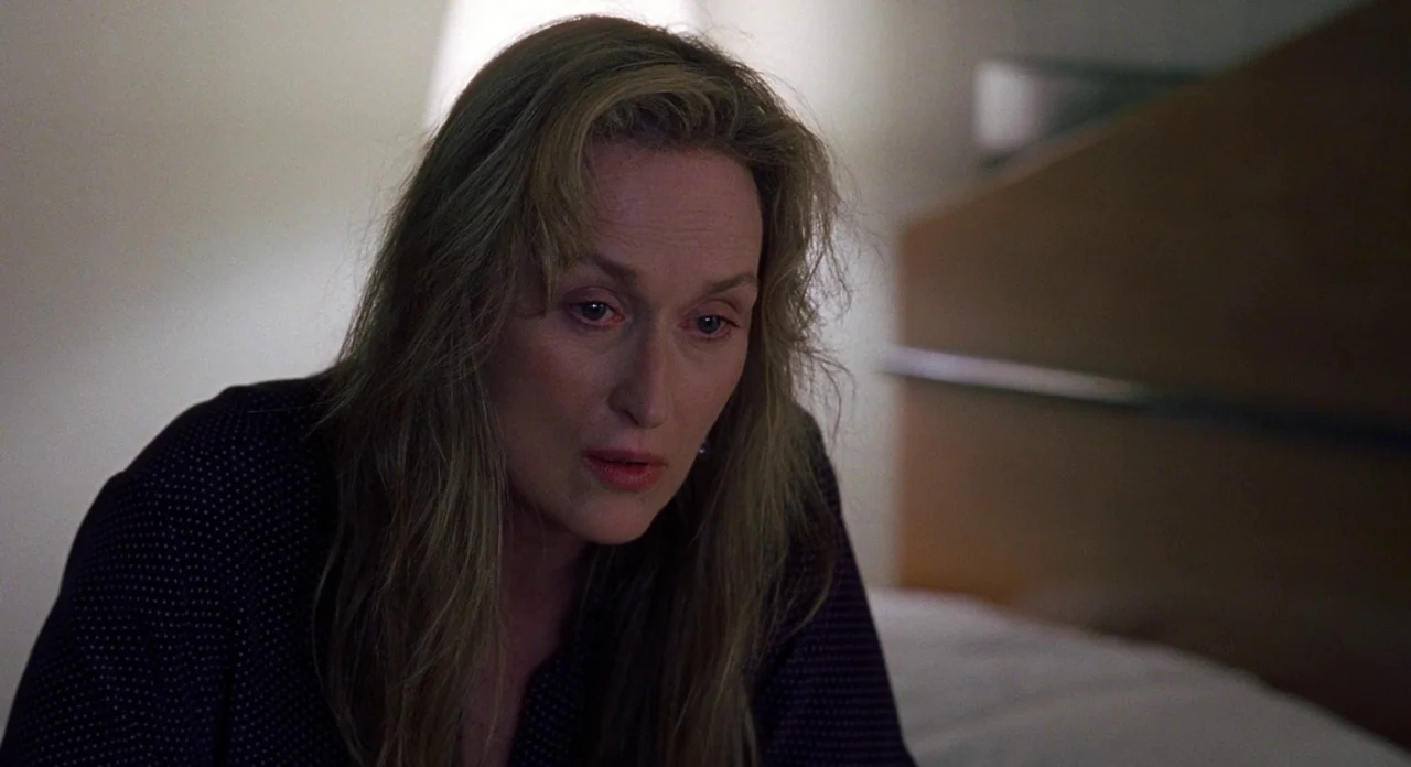 Adaptation (2002) movie still: closeup — A dimly lit indoor space with a plain wall and a headboard visible. A woman with long wavy hair sits and…