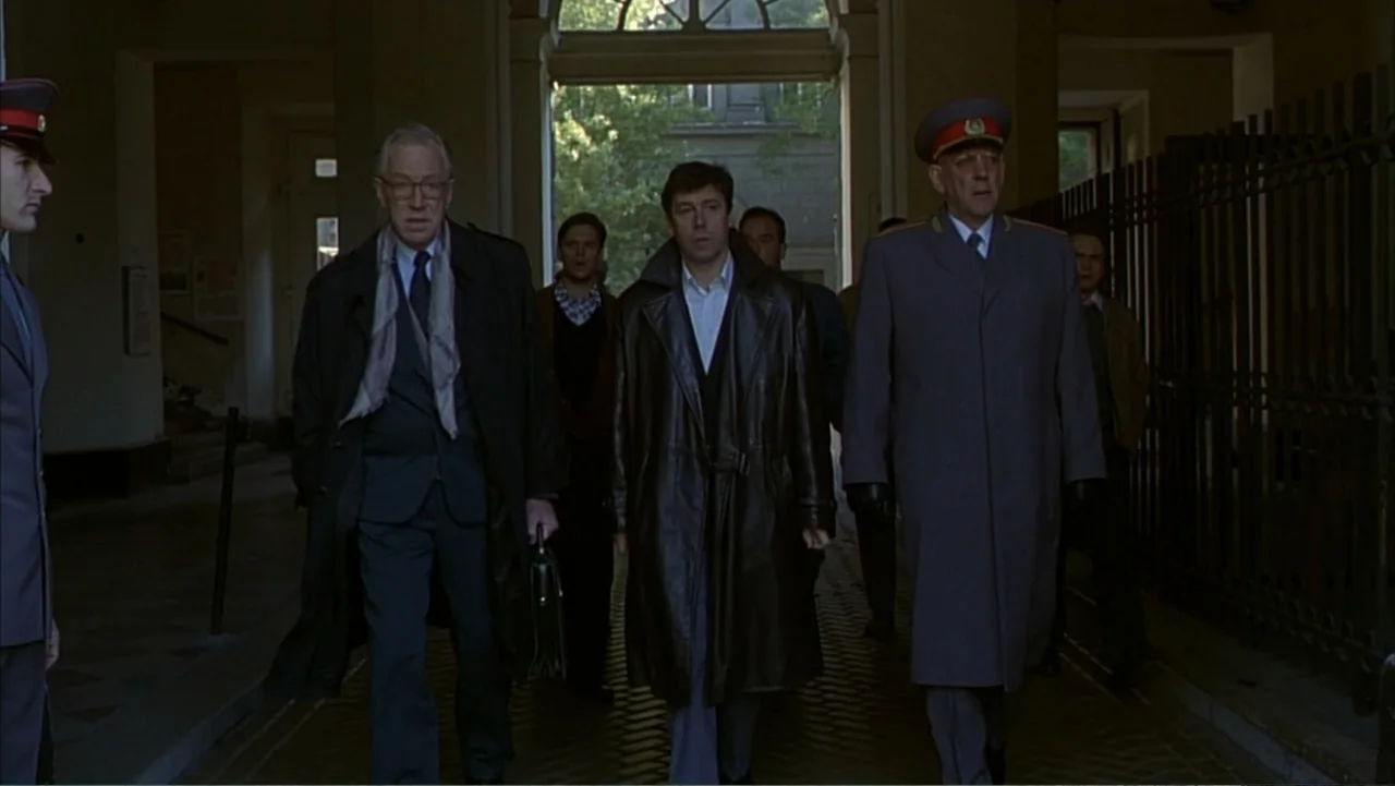 Citizen X (1995) movie still: fullbody — A stone-walled courtyard with a deep archway leading to a brightly lit exterior. Three men walk in a line…