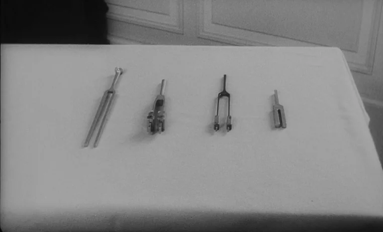 The Wild Child (1970) movie still: closeup — A white tablecloth covers a flat surface supporting four distinct metal tuning forks. The objects are…