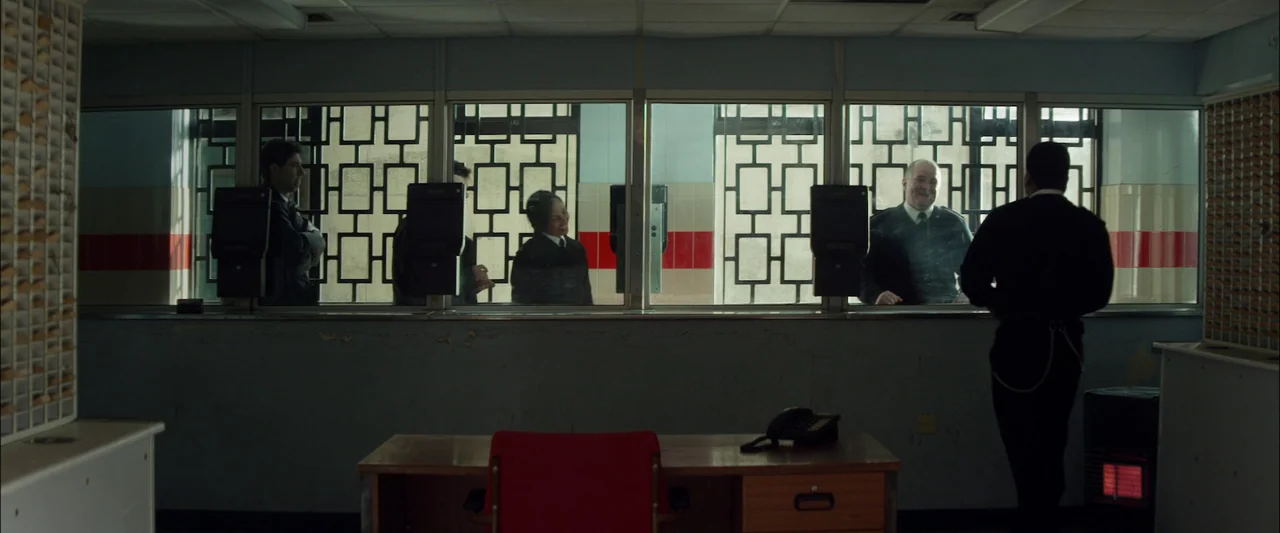 Starred Up (2013) movie still: wide — A security office with a large multi-pane window featuring decorative iron security grilles. Several uniformed…