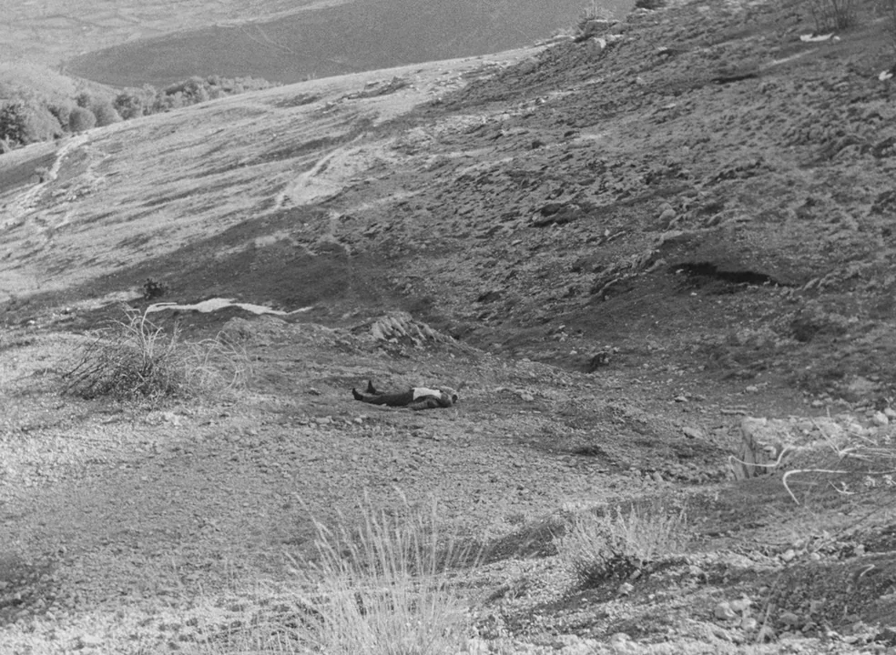 Il Bidone (1955) movie still: establishing — An expansive, barren hillside covered in loose gravel and sparse vegetation. A single figure lies…