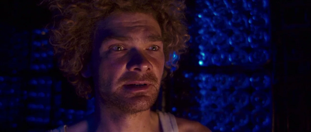 Bunny and the Bull (2009) movie still: closeup — A man stands in an unidentifiable dark room illuminated by a strong blue light source. He looks…