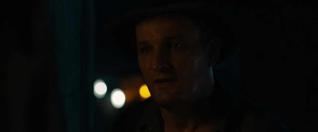Mudbound (2017) movie still: closeup — A dimly lit, dark space obscures the background, showing only blurred lights in the distance. A man wearing a…