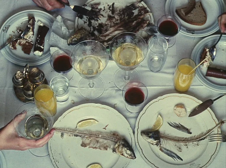 Daisies (1966) movie still: establishing — A white tablecloth is cluttered with partially eaten food, wine glasses, and fish remains. Multiple…
