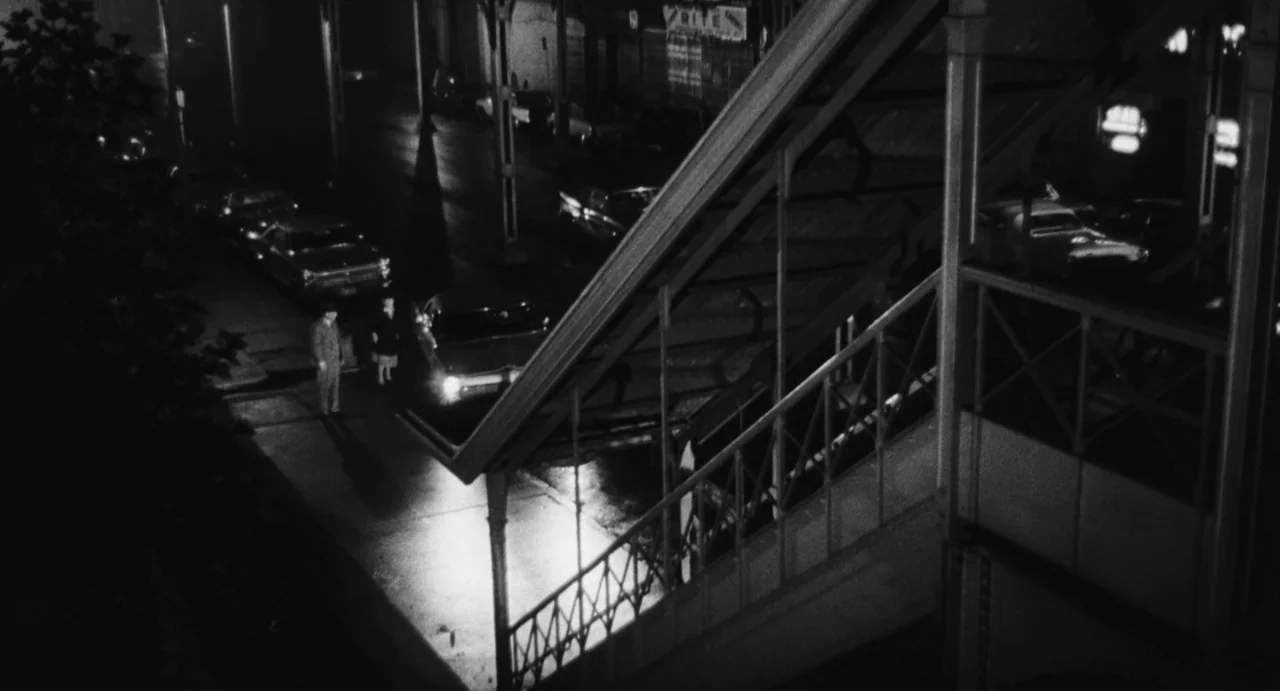 The Incident (1967) movie still: wide — An urban setting features a metal staircase structure beside a dark paved street. Parked cars line the road…