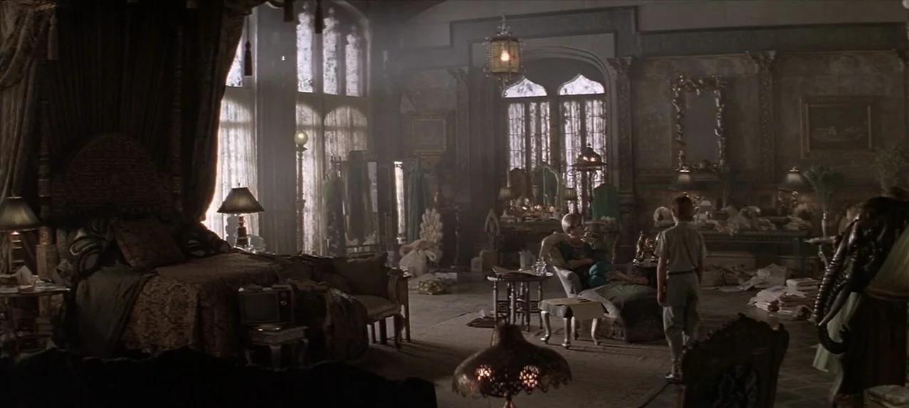 Great Expectations (1998) movie still: wide — A cluttered, Victorian-style bedroom with a massive canopy bed and tall arched windows. An elderly…