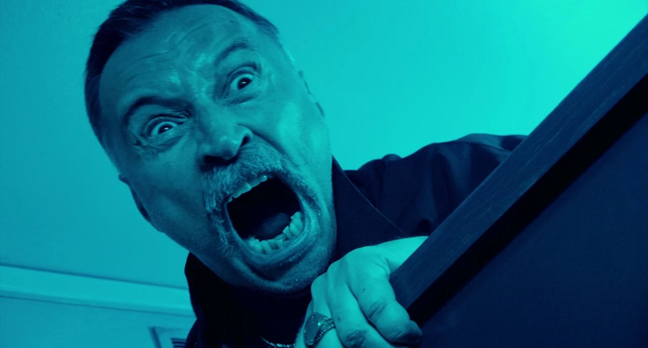 T2 Trainspotting (2017) movie still: closeup — A man screams in a darkened indoor space lit by a stark blue light. He grips a dark angular surface…