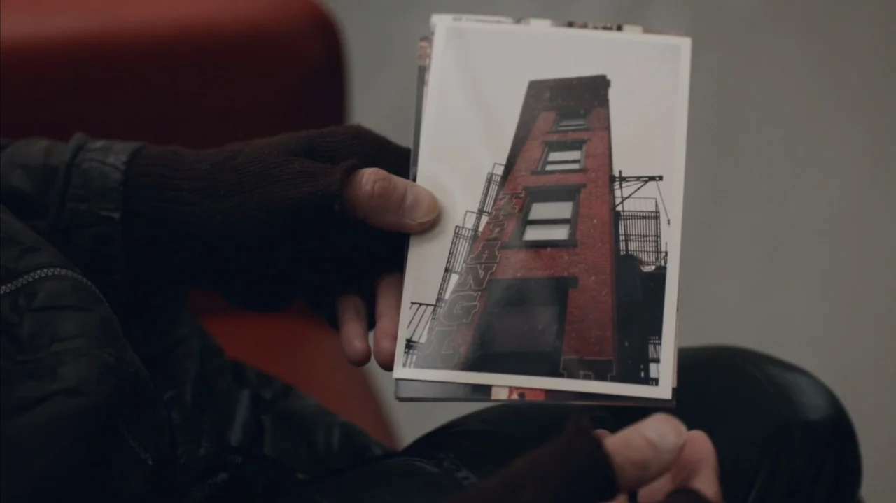 The Stroll (2023) movie still: closeup — A person holds a small printed photograph in their hands. The person wears dark fingerless gloves and a…