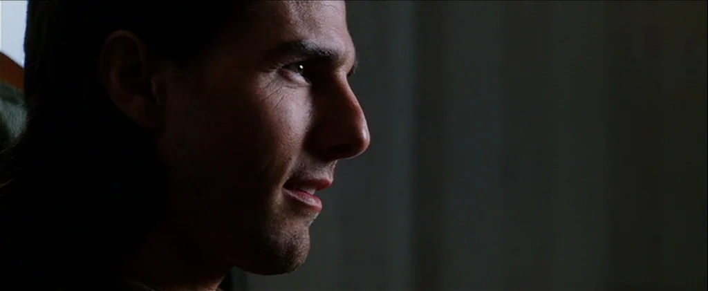 Magnolia (1999) movie still: closeup — A dimly lit indoor space with a dark, indistinct background. A man sits with his side profile to the camera.