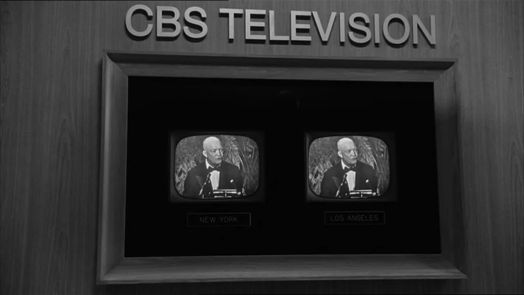 Good Night And Good Luck (2005) movie still: medium — A wall-mounted display panel shows two television sets labeled New York and Los Angeles. Both…