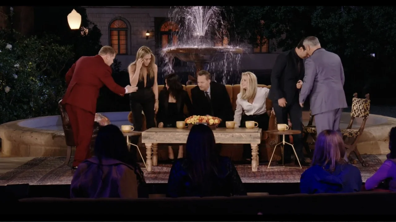 Friends: The Reunion (2021) movie still: wide — A television talk show stage features a fountain behind a couch and coffee table. Six individuals…