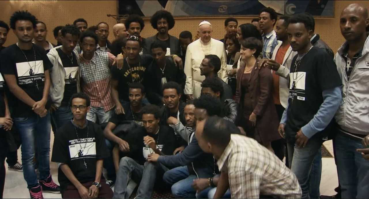 Pope Francis: A Man of His Word (2018) movie still: medium — A crowded interior hall features a large gathering of men posing for a photograph. Pope…