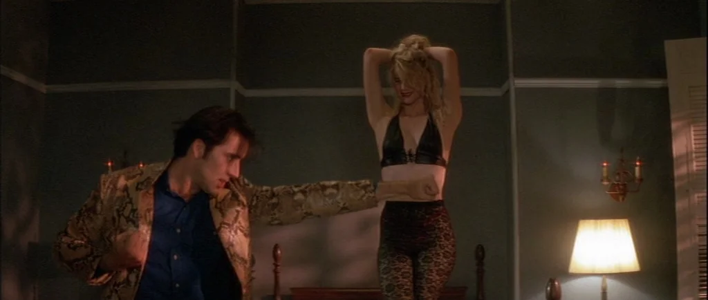 Wild At Heart (1990) movie still: medium — A dimly lit room with muted green walls and a single warm table lamp. A man and woman dance together in…
