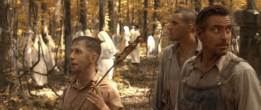 O Brother, Where Art Thou? (2000) movie still: medium — An autumnal woodland with tall trees and many white-robed figures standing in the…