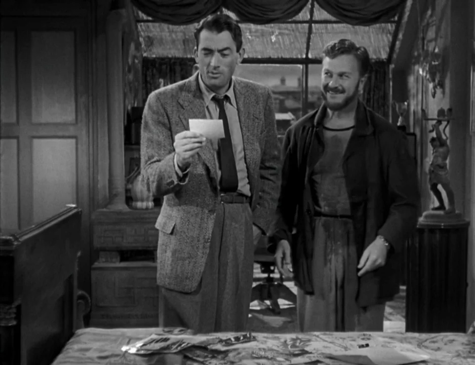Roman Holiday (1953) movie still: medium — An interior space with draped walls and decorative statues on side tables. Two men stand together while…