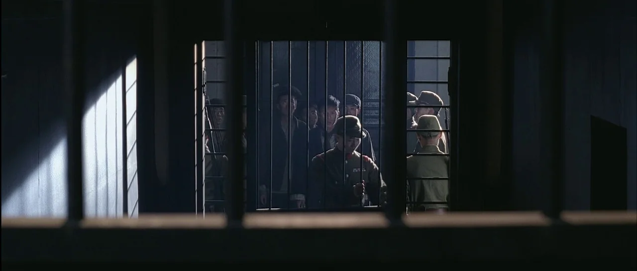 Ip Man (2008) movie still: medium — A dark space viewed through heavy vertical iron bars. Several men in military and civilian clothes stand inside…
